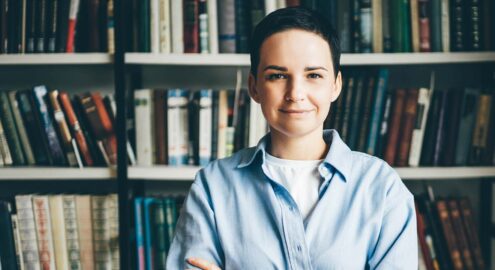 Young woman standing in front of bookshelves. Education concept.