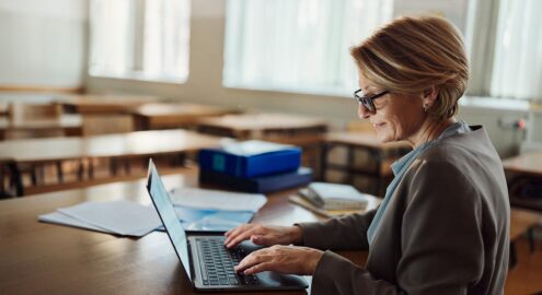 Smiling mature female teacher working on a computer at high school.